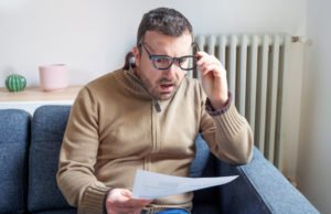 Man on couch looking at a paper bill in surprise